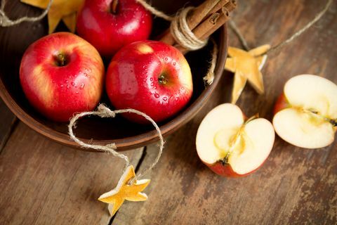 בשלים תפוחים אדומים טריים בקערה עם קינמון על רקע עץ. קציר סתיו. קישוט חג המולד