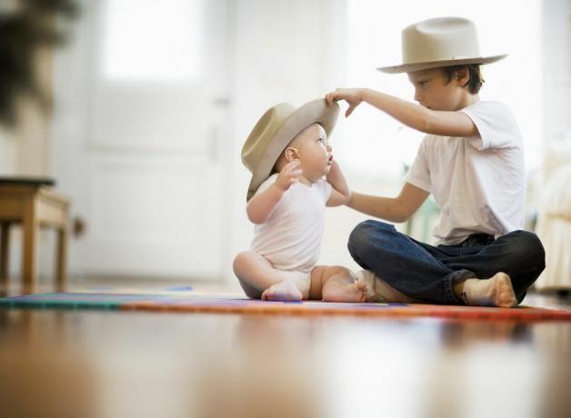 מיקוד סלקטיבי של שני אחים, אחד בן תשע אחד הוא שמונה חודשים הזוג יושב ברגליים שלובות על הרצפה ילד מבוגר שם כובע תואם על ראשו של התינוק