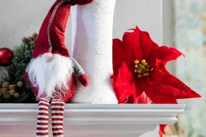 קישוט גמד חג המולד של חג נורווגי יושב על מעטה מודרני לבן עם אגרטל לבן עם אקליפטוס ופריחה של פוינסטיה