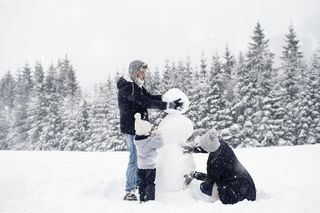 משפחה בת שלוש נפשות בונה איש שלג בשלג