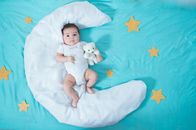 תינוקת לטינית יפהפייה, בת חודשיים, שוכבת על סדין לבן בצורת ירח עם כוכבים צהובים בכל צד וסדין כחול מתחת להכל