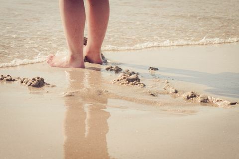 צילום מקרוב של רגליה של האישה ביד בחוף הים - הים נכנס