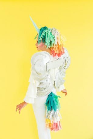 אישה לבושה כחלק מפגסוס, חלקה חד קרן עם זנב ורעמת נייר צבעונית, כנפיים לבנות וקרן לבנה
